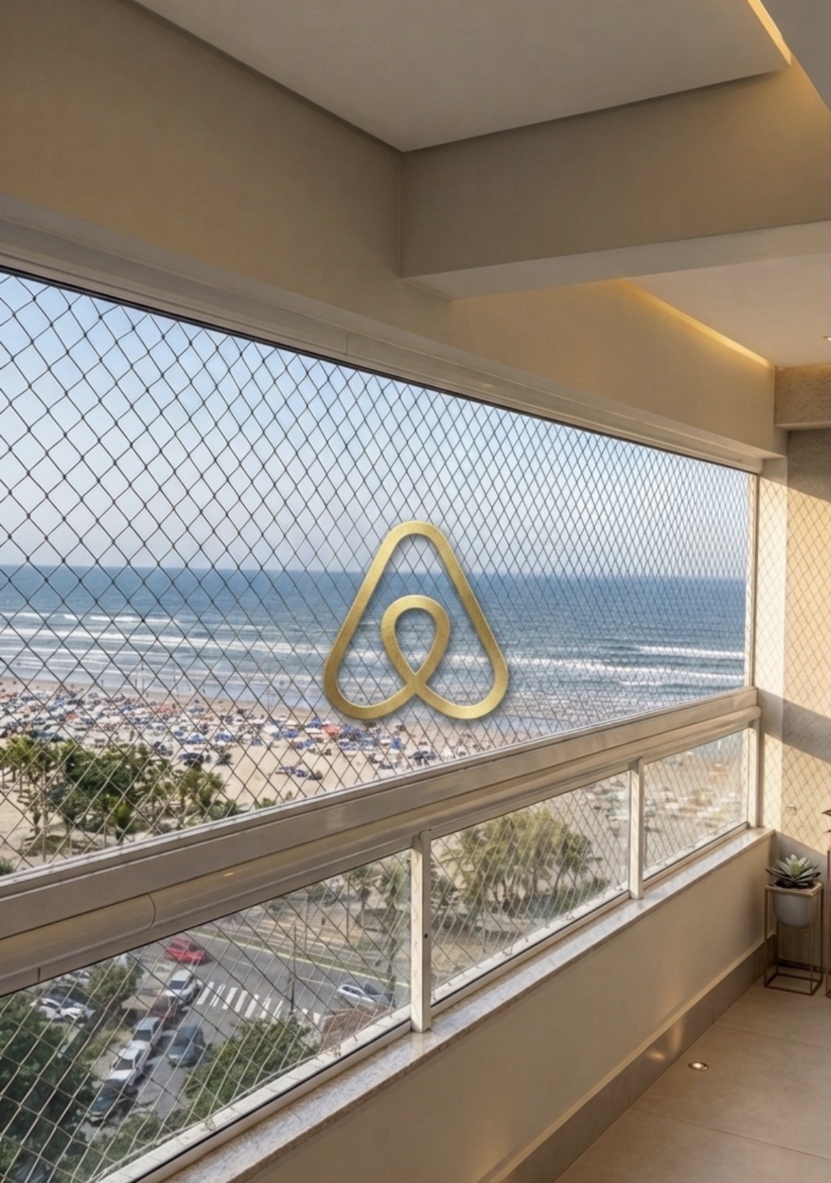 Varanda envidraçada do apartamento Maré com vista para o mar de Praia Grande e símbolo Airbnb em latão dourado no vidro.