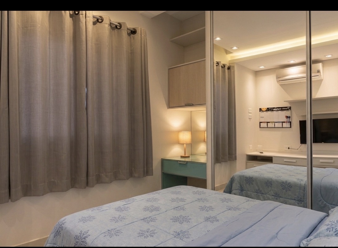 Quarto com cortina de linho cinza, cama de casal com edredom azul-gelo estampado e guarda-roupa espelhado.