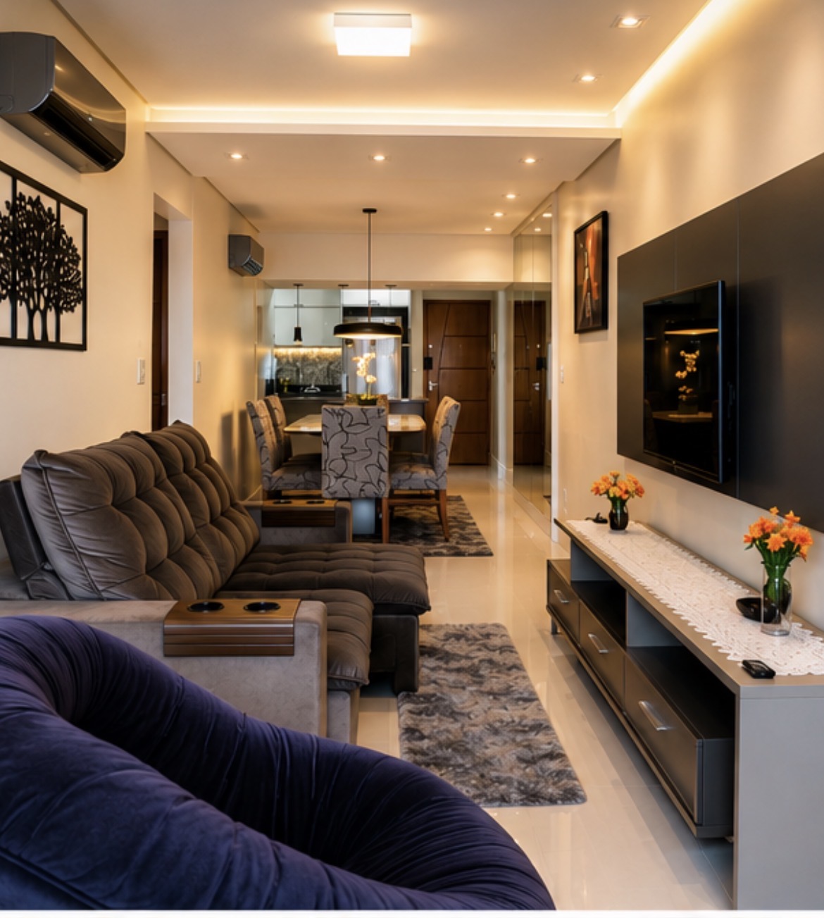Sala de estar do apartamento Maré com sofá modular grafite tufado, poltrona em veludo aubergine em primeiro plano, TV em painel escuro e mesa de jantar ao fundo.