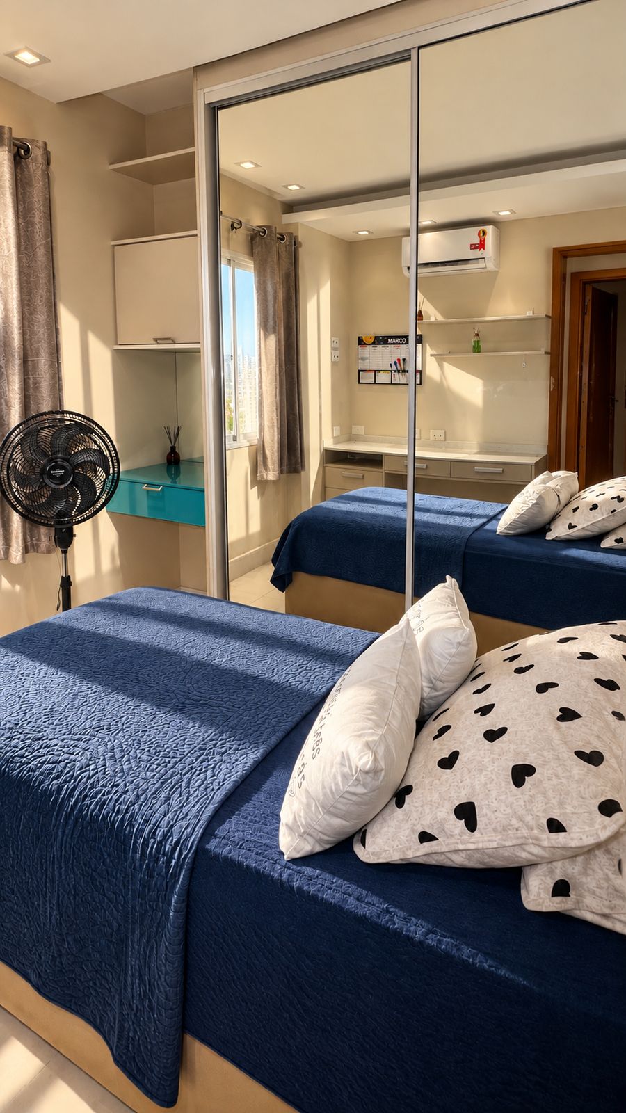Segundo quarto real do Maré, com duas camas, guarda-roupa espelhado e espaço de trabalho.